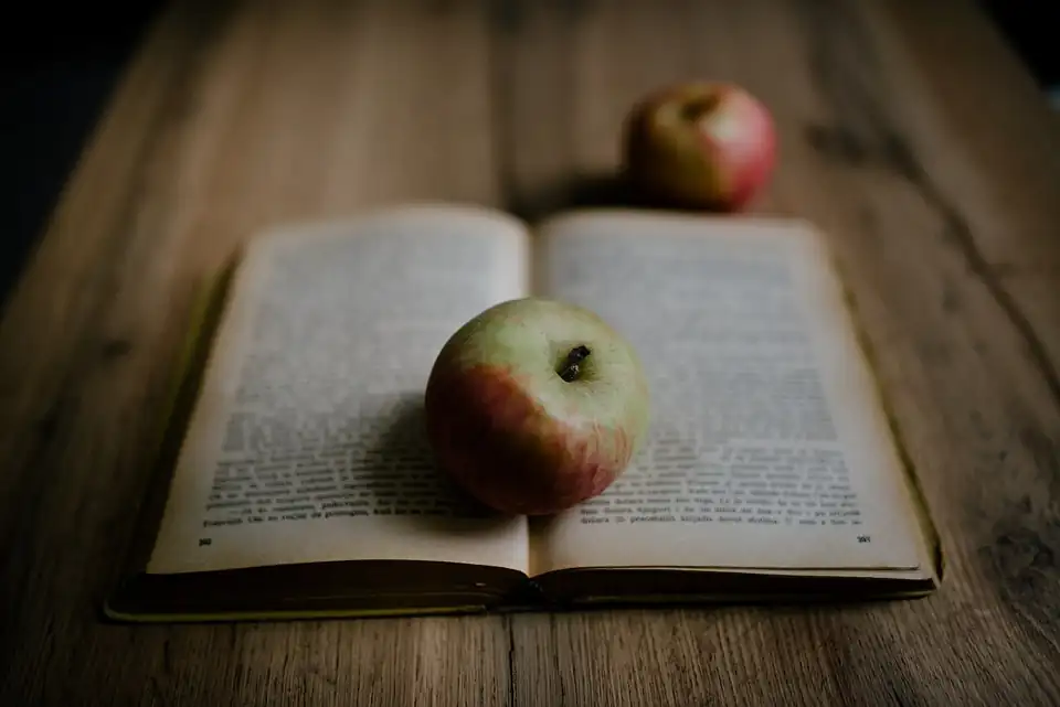 Photo: Open book with apples placed on a wooden table in a bright indoor setting