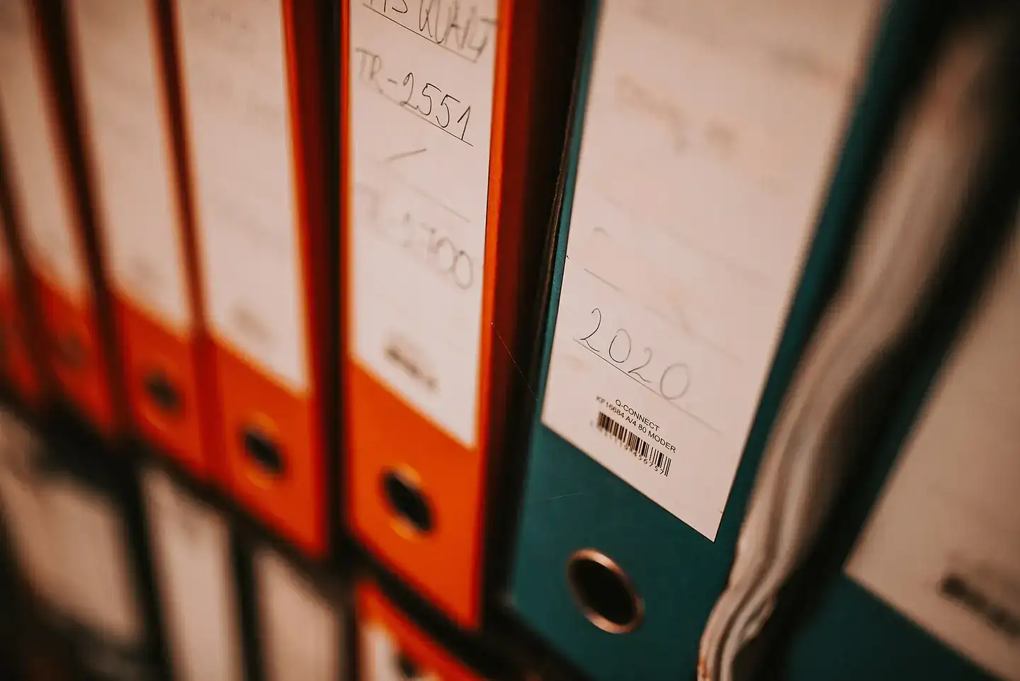 Several binders in orange and green are lined up on a shelf